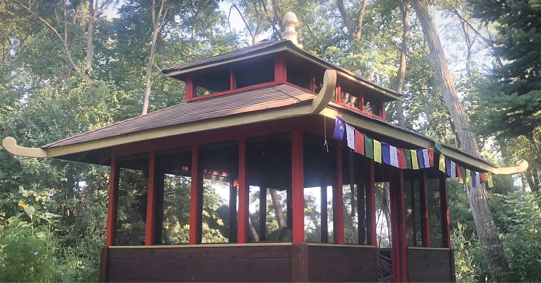 The Gaia Temple at SoderWorld, an open wooden pavilion hung with prayer flags among the trees